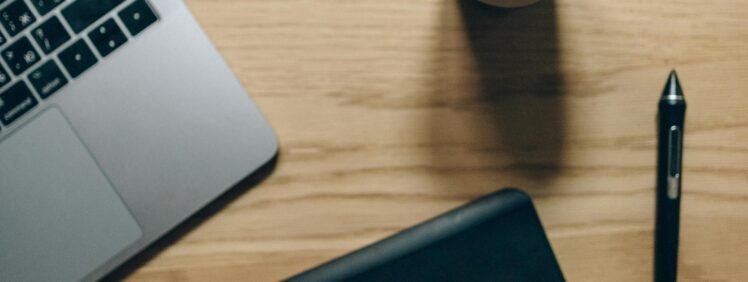 Overhead view of a workspace with laptop, pen, and coffee on a wooden table.